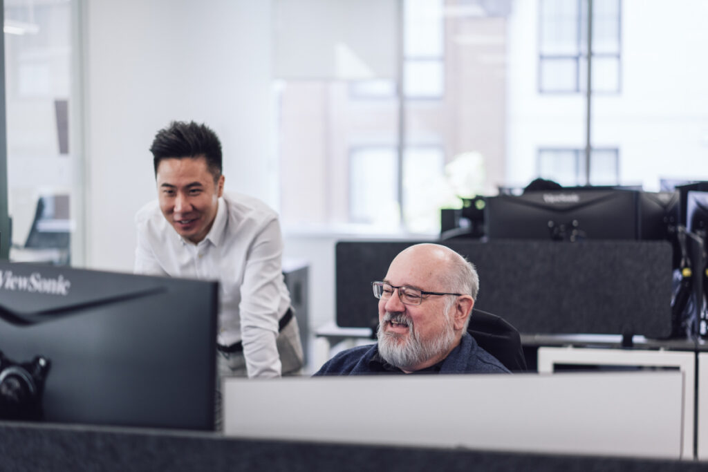 Two coworkers talk about work at one of their workstations