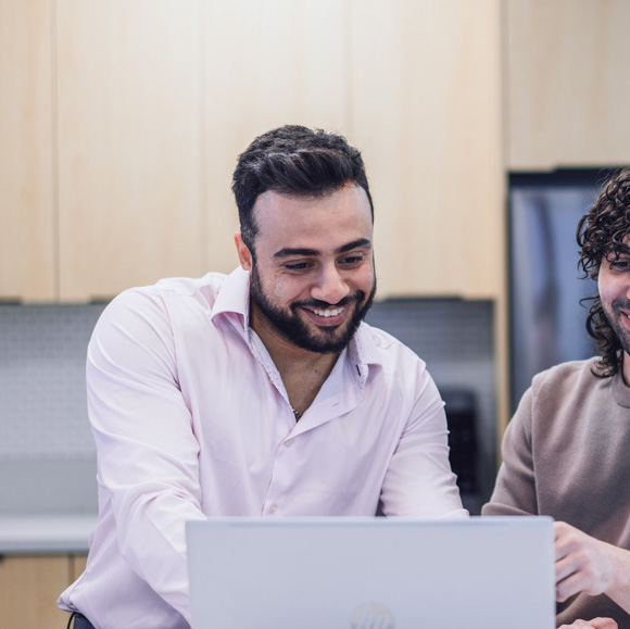 An employee beside their coworker looking at a laptop