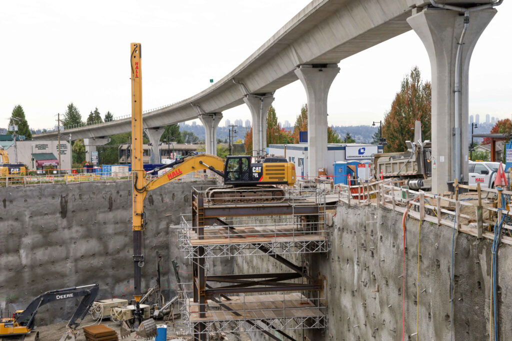 A hall construction crane in a pit below the sky train line