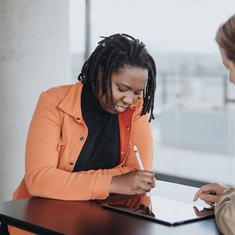 An employee sitting at a table with a coworker drawing on a tablet
